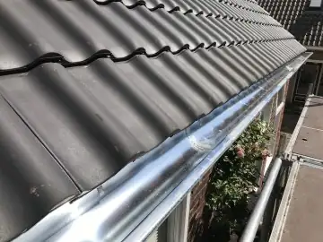 Zinken dakgoot langs zwarte dakpannen